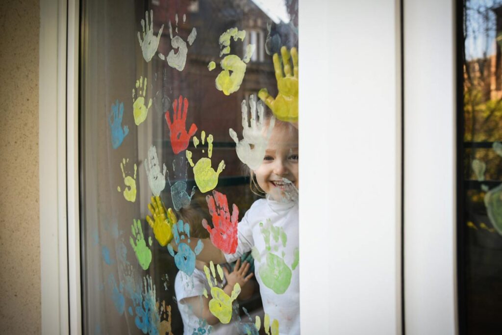 Grupka dzieci odbija umoczone w farbie dłonie na szybie okna