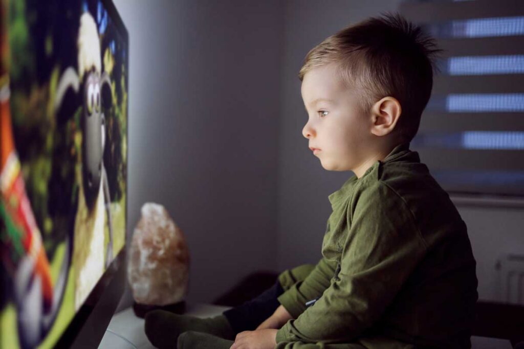 Małe dziecko siedzące zbyt blisko ekranu telewizora i patrzące na niego z dużą ciekawością