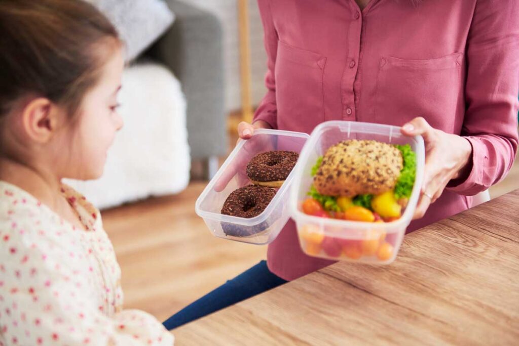 Mama daje dziewczynce wybór pomiędzy zdrową kanapką z warzywami a pączkami