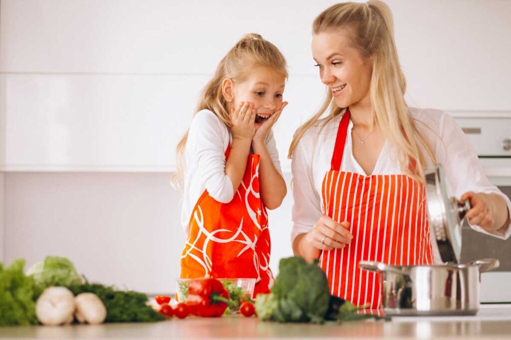 Mama z córką ubrane w czerwone fartuszki wspólnie gotują zdrowe danie