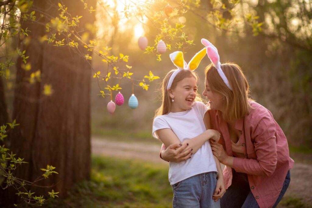 mama z córką mające na głowach pluszowe królicze uszy dobrze się bawią w ogrodzie udekorowanym na Wielkanoc